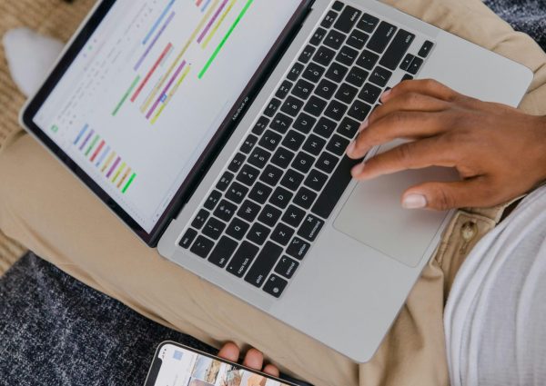 Man sitting on sofa multitasking with laptop and phone, focused on digital projects.